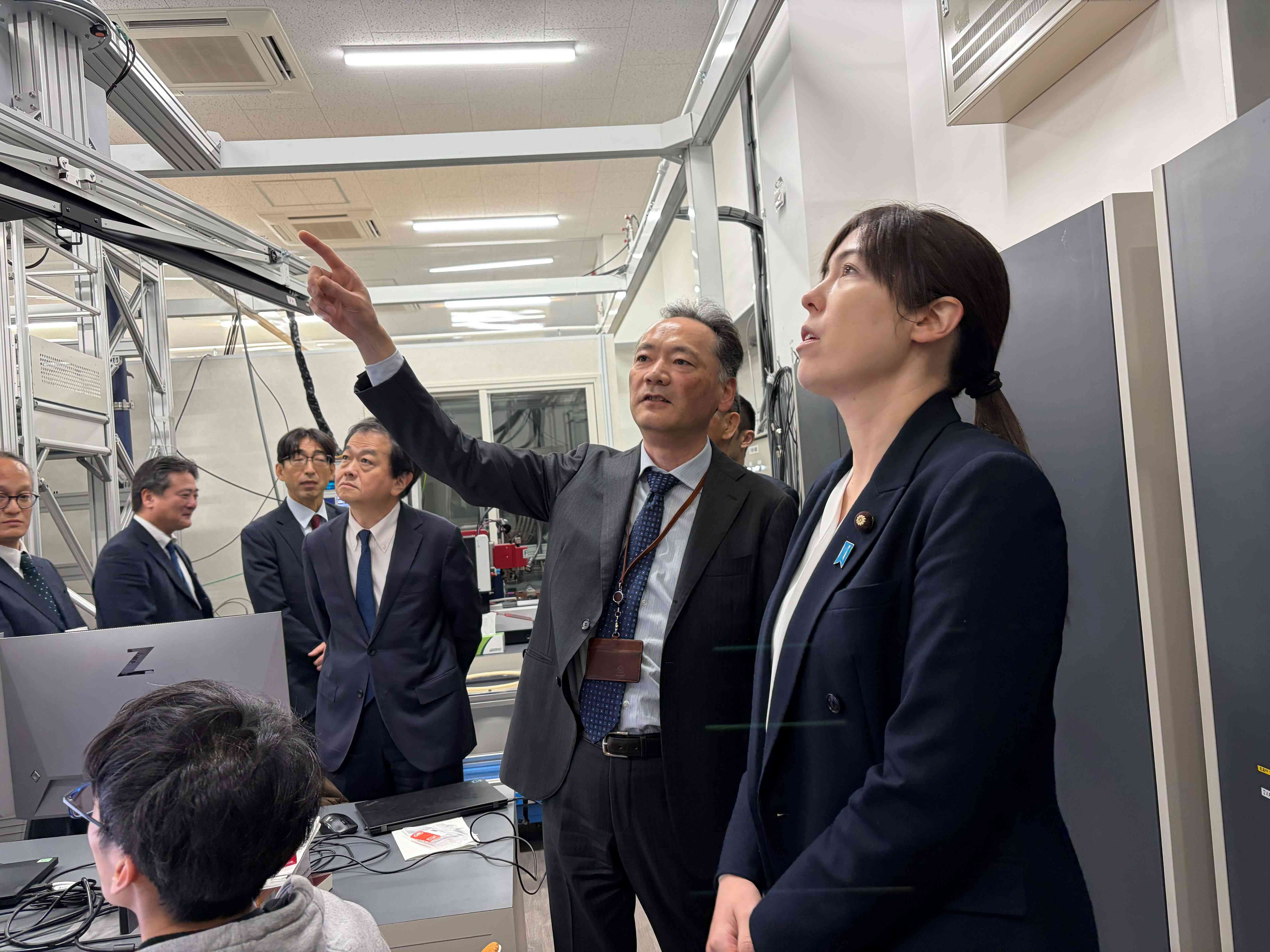 日立協創の森の研究設備前で説明を受ける小野田大臣ら。