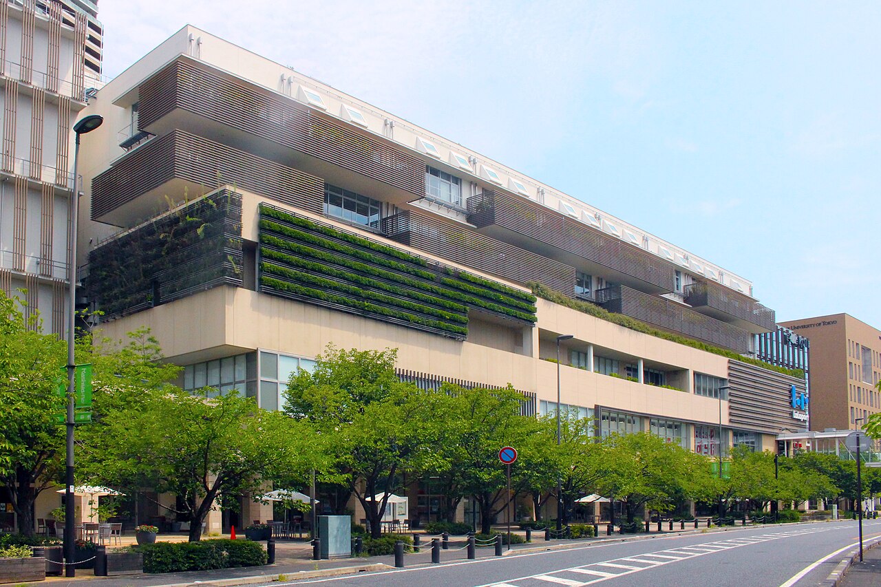 KOILのロゴが付いたガラス張りの建物。下層部にららぽーと柏の葉北館、手前に芝生と通路がある。