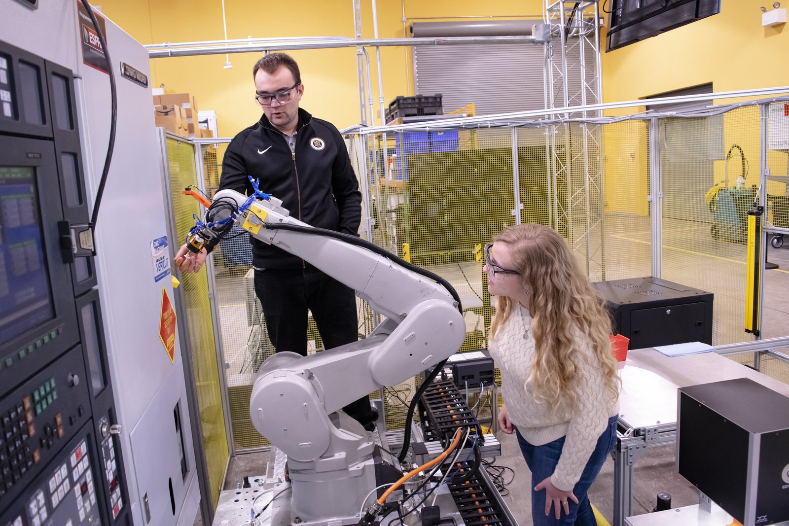MxDの工場フロアに設けられたDiscrete Manufacturing Testbedで、産業用ロボットと生産設備を案内する技術者。